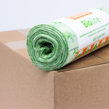 Eine Rolle grüner Biomüllbeutel wird auf einen Karton gelegt. Das Etikett auf der Rolle ist teilweise sichtbar und trägt den Aufdruck „EMIL DEISS KG (GmbH + Co.).“ Diese 100% kompostierbaren Beutel haben ein florales Design und sind 430 x 500 mm groß.