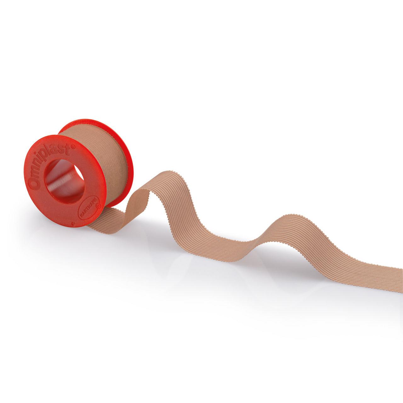 Un rotolo di nastro adesivo Hartmann Omniplast® beige con un dispenser rosso con la scritta "Paul Hartmann AG" su sfondo bianco. Il nastro si srotola ondulato verso il lato destro del dispenser.