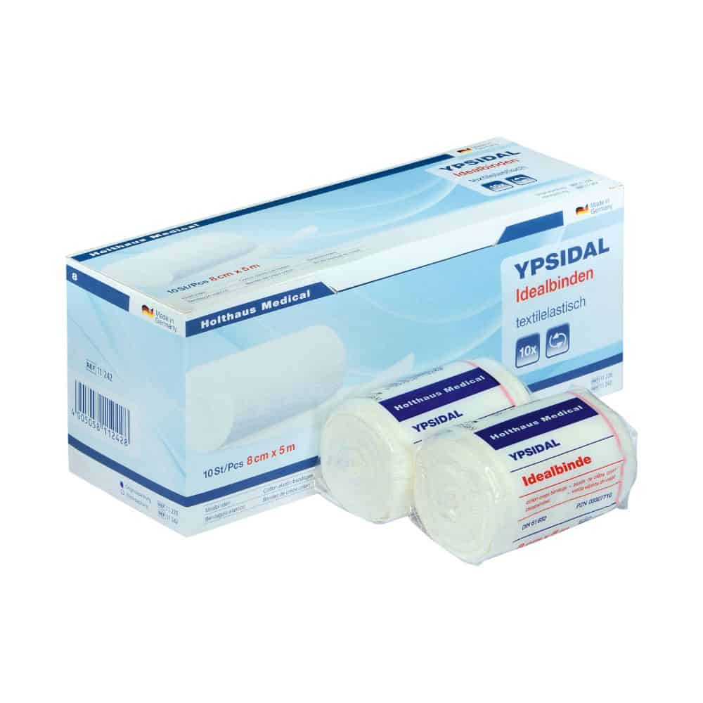 Una scatola bianco-blu con la scritta "Holthaus Medical YPSIDAL Idealbinde" di Holthaus Medical GmbH & Co. KG con due rotoli di bende elastiche sulla parte anteriore. I rotoli sono avvolti in pellicola di plastica e riportano una scritta simile. La confezione contiene un testo tedesco con la scritta "benda elastica per compressione" e immagini di bende arrotolate.