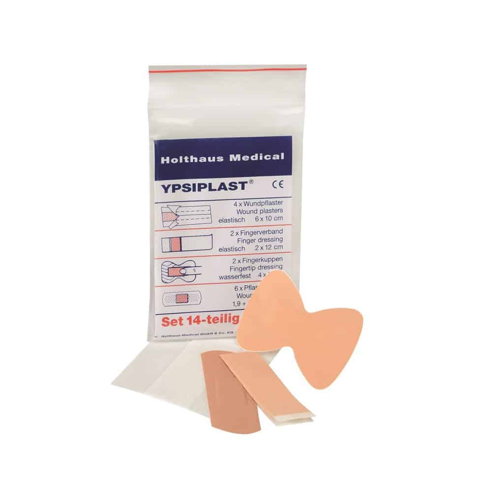 Nella foto è raffigurata una confezione di cerotti Holthaus Medical YPSIPLAST® set, DIN della Holthaus Medical GmbH & Co. KG. Il set da 14 pezzi include 4 cerotti per ferite (6 x 10 cm), 2 cerotti per punte delle dita e fasce per le dita, 2 cerotti a farfalla e 6 piccoli cerotti adesivi. Alcuni degli articoli sono raffigurati fuori dalla confezione.