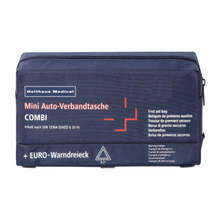 Una borsa di pronto soccorso blu marino con la scritta „Holthaus Mini Combi Auto-Verbandtasche“ di Holthaus Medical GmbH & Co. KG, con una croce bianca e dettagli rossi. Il testo contiene diverse traduzioni di „borsa di pronto soccorso“ e menziona che il contenuto è conforme alla norma DIN 13164.