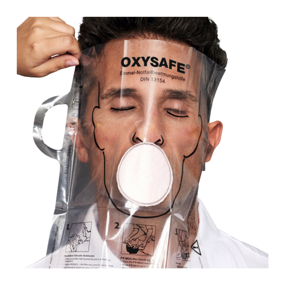 Una persona indossa una maschera per la rianimazione d'emergenza trasparente Holthaus Oxysafe® della Holthaus Medical GmbH & Co. KG e tiene gli occhi chiusi, mentre un'altra persona adatta la maschera. Il prodotto è dotato di istruzioni e diagrammi stampati sulla superficie di plastica.