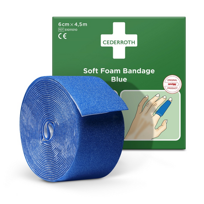Davanti a una scatola di confezione verde viene presentato un rotolo di cerotto in schiuma morbida blu Holthaus con la scritta 6 cm x 4,5 m. La scatola mostra una mano con la benda avvolta attorno a un dito e porta la scritta 'Cederroth Weichschaumverband Blau'. Questo prodotto si adatta perfettamente al rotolo di ricarica in schiuma morbida di Holthaus Medical GmbH & Co. KG.