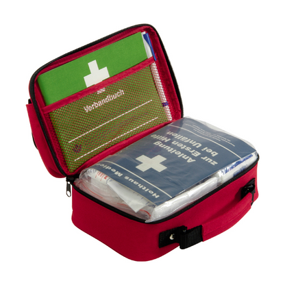 Una compatta borsa di pronto soccorso rossa Holthaus Office plus, DIN 13 157 di Holthaus Medical GmbH & Co. KG, con manico nero che si apre per rivelare il contenuto. All'interno ci sono un manuale di istruzioni verde e una borsa di pronto soccorso Holthaus blu, decorata con una croce bianca e testo tedesco. L'attrezzatura di pronto soccorso è organizzata in modo ordinato in tasche a rete e scomparti, rendendola quindi ideale per ambienti d'ufficio.