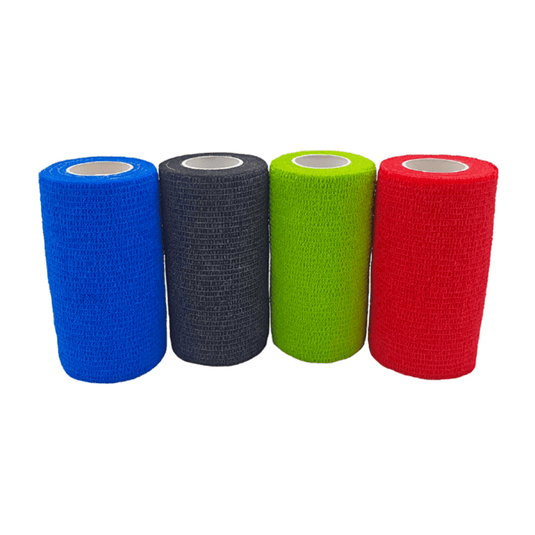 Quattro rotoli di bendaggio autoadesivo Holthaus VliVet® per uso veterinario, prodotti da Holthaus Medical GmbH & Co. KG, sono allineati uno accanto all’altro. Da sinistra a destra, i colori sono blu, nero, verde e rosso. I bendaggi presentano una superficie strutturata e una forma cilindrica con un’anima interna bianca, ideali per la cura degli zoccoli in ambito veterinario.