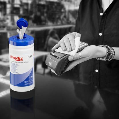 Qualcuno utilizza una salvietta per la disinfezione delle superfici WypAll® (Kimberly-Clark GmbH) da una vaschetta dispensatrice aperta per disinfettare un terminale per carte. Il secchio dispensatore bianco (200 salviette) è sul bancone, lo sfondo è sfocato.