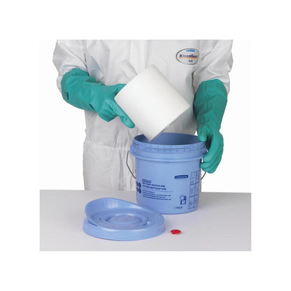 Una persona con guanti verdi e tuta bianca inserisce un rotolo di salviette Kimtech® Wettask™ in un secchio dispenser blu della Kimberly-Clark GmbH; il coperchio e il tappo rosso sono appoggiati sul tavolo accanto.