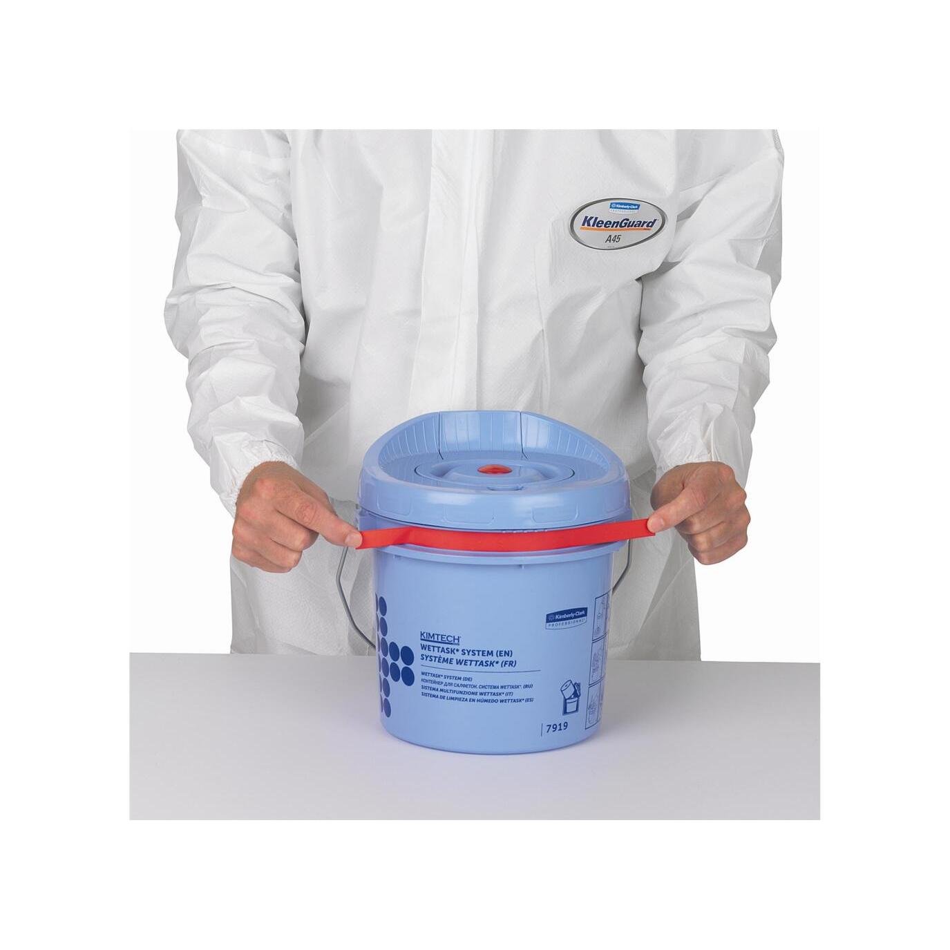 Una persona in una tuta bianca KleenGuard tiene un secchio dispenser per salviette a rotolo Kimtech® Wettask™ blu di Kimberly-Clark GmbH (secchio di pulizia) con un manico rosso su una superficie bianca.