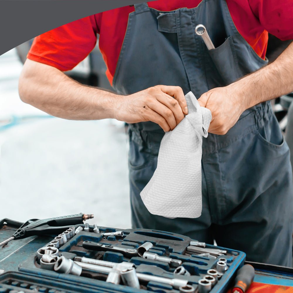 Una persona in rosso e grigio utilizza i panni di pulizia WypAll® X80 PowerClean (BRAG™ Box, Bianco, 1x160 fogli) della Kimberly-Clark GmbH su un banco di lavoro pieno di attrezzi - ideale per la pulizia industriale impegnativa.