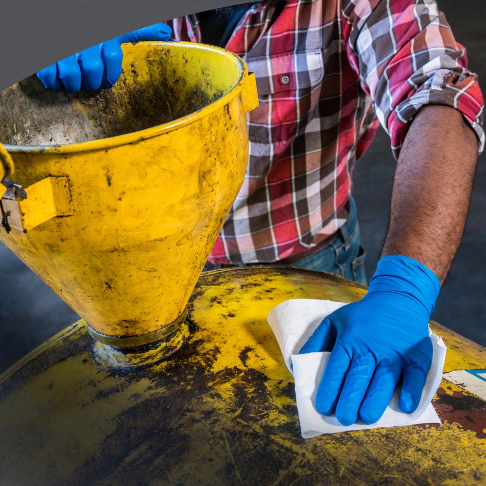 Una persona con guanti blu e una camicia a quadri utilizza i panni di pulizia WypAll® X80 PowerClean (BRAG™ Box, Bianco, 160 panni) della Kimberly-Clark GmbH per pulire un barile giallo con un panno bianco e un imbuto montato, garantendo così una pulizia industriale ottimale.