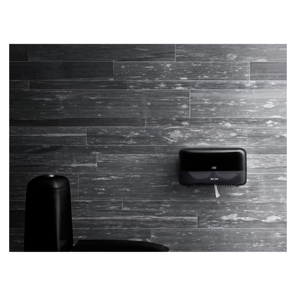 Un bagno moderno con pareti strutturate in grigio scuro presenta un distributore di asciugamani di carta Tork di alta qualità montato a parete in nero e offre parzialmente una vista su un elegante cestino nero in primo piano, mantenendo al contempo un design ecologico.