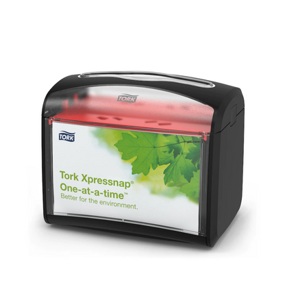 Il distributore da tavolo Tork Xpressnap® 272611 per tovaglioli di TORK – Essity Professional Hygiene Germany GmbH ha una parte superiore nera e una parte frontale trasparente con un design a foglia verde e la scritta "Tork Xpressnap One-at-a-time – meglio per l'ambiente". Questo distributore migliora l'igiene riducendo contemporaneamente in modo efficiente il consumo di tovaglioli.
