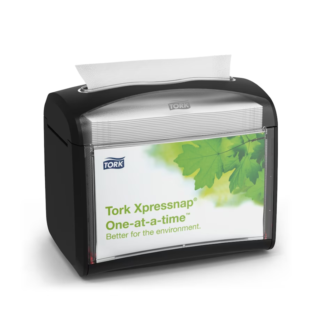 Un distributore da tavolo Tork Xpressnap® 272611 nero per tovaglioli, distribuito da TORK – Essity Professional Hygiene Germany GmbH, è presentato con un'etichetta con foglie verdi e il messaggio "Singolarmente. Meglio per l'ambiente". Un singolo tovagliolo viene erogato parzialmente dall'alto per promuovere l'igiene e un consumo efficiente dei tovaglioli.