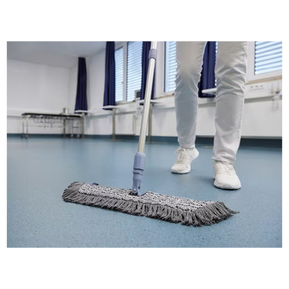 Una persona con scarpe e pantaloni bianchi pulisce un pavimento blu con un Vileda GmbH Professional Swep Duo r-MicroCombi Mop - 50 cm in una stanza con persiane chiuse e tende blu. Vicino ci sono un tavolo pieghevole e un radiatore sotto le finestre.