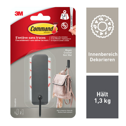 Eine Packung von 3M Deutschland GmbH mit 1 mittelgroßer Command™ mattschwarzer Haken (17034B) und 2 Strips; hält bis zu 1,3 kg, kein Bohren erforderlich. Inklusive schwarzem Wandhaken, Klebestreifen und einem Beispielbild; Infos auf Französisch & Deutsch.