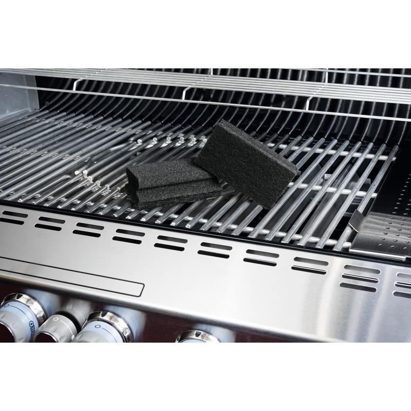 Una spugna Scotch-Brite® Grill di 3M Deutschland GmbH è posizionata su una griglia in acciaio inossidabile e sottolinea la facilità di pulizia della griglia. Sulla griglia sono visibili le spugne nere, i pomelli della griglia e il coperchio aperto.