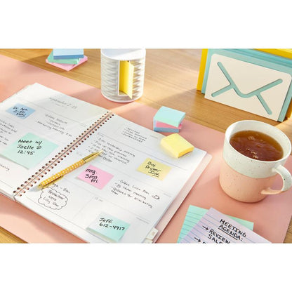 Un planner aperto con note scritte a mano si trova su una scrivania, circondato da una penna, tè, schede, un organizzatore di posta e foglietti adesivi Post-it® Recycling Z-Notes (76 mm x 76 mm, 100 fogli/blocco, 100% PEFC) della 3M Deutschland GmbH.