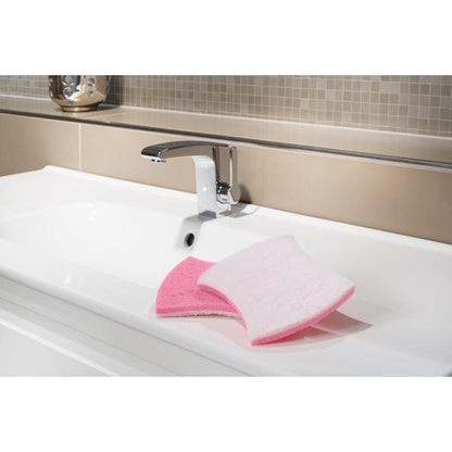 Un lavabo bianco con un rubinetto cromato mostra la spugna per la pulizia del bagno Scotch-Brite® Bath XXL di 3M Deutschland GmbH, rosa da un lato e bianca dall'altro, ideale per rimuovere i depositi di calcare. Sullo sfondo appaiono piastrelle beige e marrone chiaro.