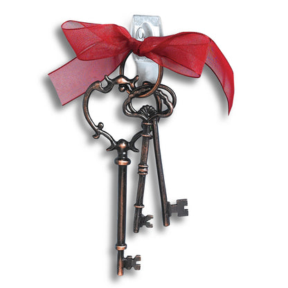 Drei mit einer roten Schleife gebundene Schlüssel im Vintage-Stil werden auf weißem Hintergrund an einem transparenten 3M Command™ Mini-Haken (17006CLR) aufgehängt. Die mitgelieferten Strips ermöglichen einfaches, spurloses Befestigen durch 3M Deutschland GmbH.