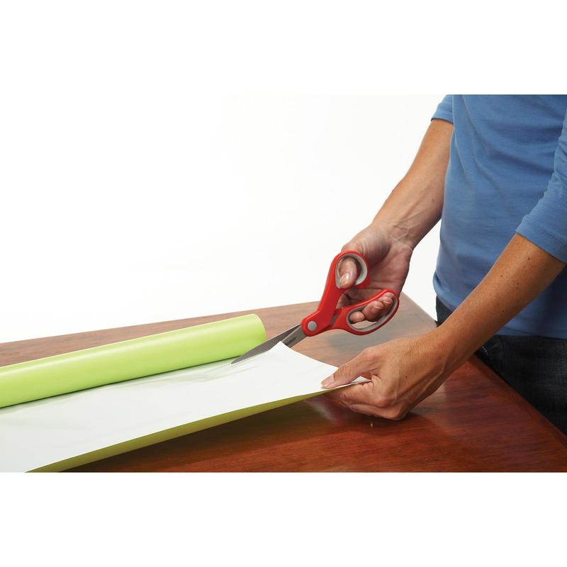 Una persona con una camicia blu usa le forbici di precisione rosse Scotch™ di 3M Deutschland GmbH per tagliare carta o vinile verde chiaro parzialmente srotolato su una superficie di legno.