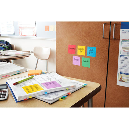 Auf dem Schreibtisch eines Klassenzimmers liegen offene Hefte, Papiere, ein Taschenrechner und Textmarker. 3M Deutschland GmbH Post-it® Super Sticky Notes (76 mm x 76 mm, 90 Blatt/Block, 100% PEFC) sind auf einem Schrank mit Themen beschriftet; im Hintergrund sind leere Stühle zu sehen.