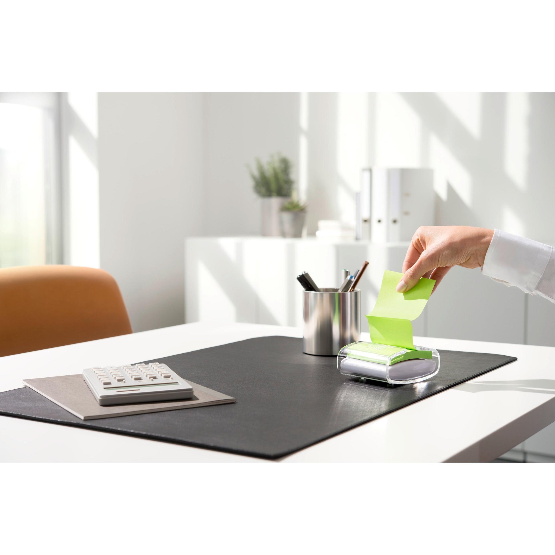 Eine Person zieht eine gelbe Post-it® Super Sticky Z-Note (76 x 76 mm) aus dem schwarzen PRO Post-it® Z-Notes Dispenser der 3M Deutschland GmbH, auf einem aufgeräumten Schreibtisch mit Taschenrechner, Stifthalter und schwarzer Unterlage bei hellem Tageslicht.