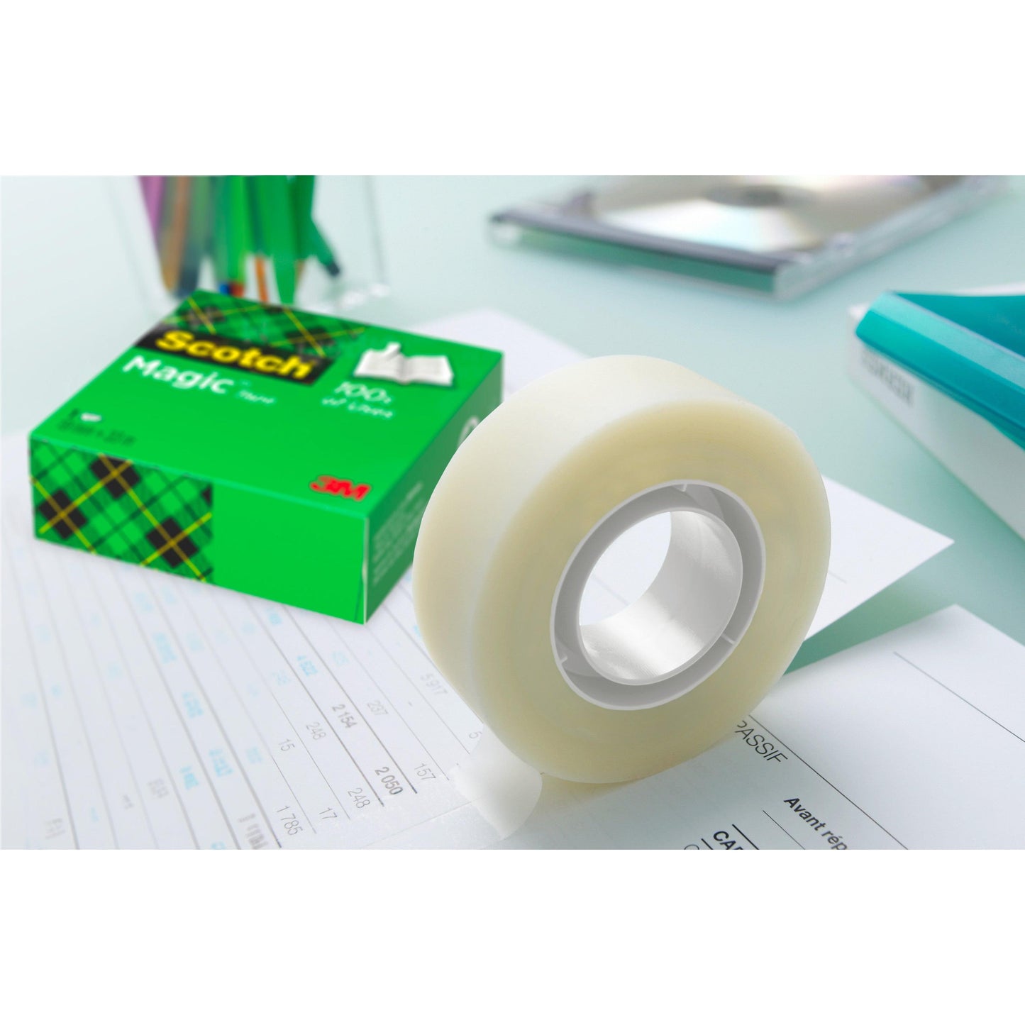 Eine Rolle Scotch® Magic™ Unsichtbares Klebeband von 3M Deutschland GmbH liegt in der grünen Schachtel auf dem Papier - ideal für jeden Schreibtisch, besonders im Vorteilspack mit 14 Rollen (19 mm x 33 m).