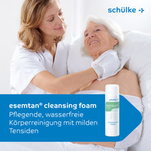 Un'infermiera in camice bianco lava delicatamente la spalla di una donna anziana a letto. In primo piano si vede una bottiglia da 500 ml della schiuma detergente Esemtan® della Schülke & Mayr GmbH, sulla quale è descritta la delicata pulizia della pelle.