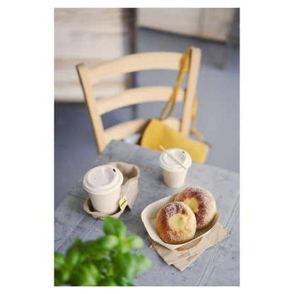 Su un tavolo ci sono due pezzi di pasticceria cosparsi di zucchero su un vassoio e due bicchieri da caffè Duni 'Sweet Bedruckte Bagasse' con coperchio di Duni GmbH. Una borsa gialla è appesa a una sedia di legno, mentre una pianta verde parzialmente visibile in primo piano evidenzia il tema sottile della sostenibilità.
